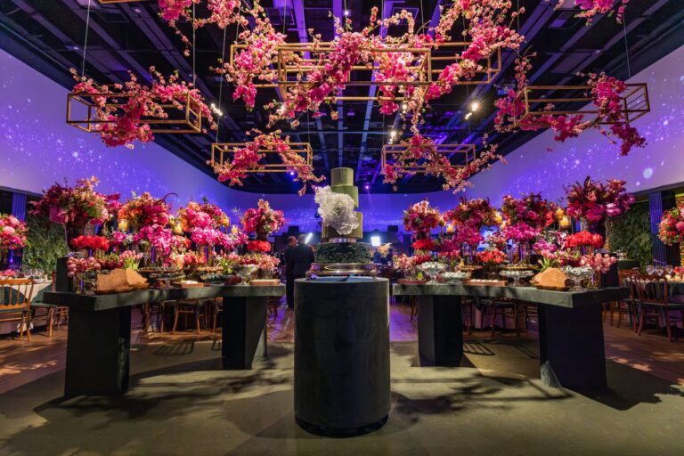 Escena de un evento de interior, con mesas con comida y flores y una estructura con flores colgando del techo